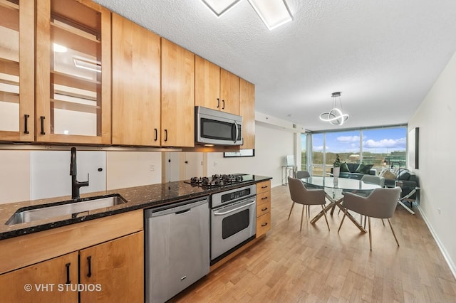 kitchen featuring a textured ceiling, a sink, appliances with stainless steel finishes, dark stone counters, and light wood finished floors