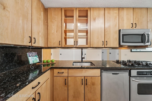 kitchen featuring glass insert cabinets, appliances with stainless steel finishes, dark stone countertops, a textured ceiling, and a sink