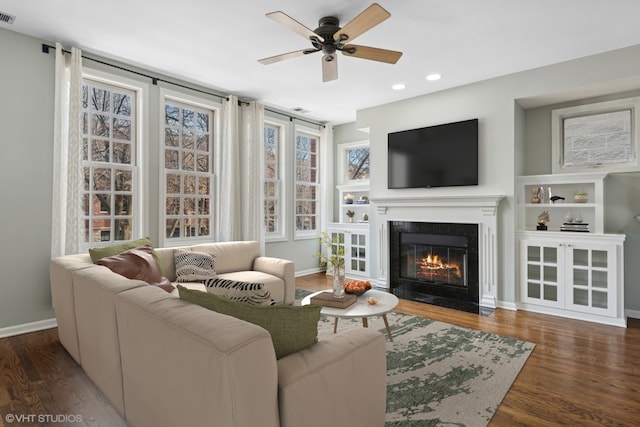 living room with a fireplace with flush hearth, baseboards, visible vents, and wood finished floors