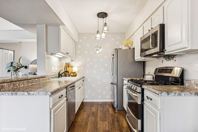 kitchen with a sink, baseboards, appliances with stainless steel finishes, dark wood-style floors, and wallpapered walls