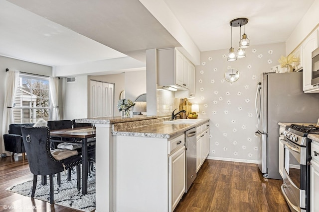 kitchen with wallpapered walls, baseboards, dark wood-style floors, stainless steel appliances, and a sink