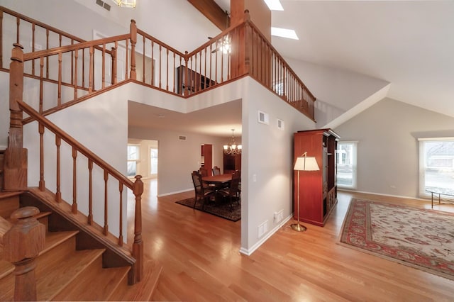 staircase with a chandelier, wood finished floors, visible vents, a towering ceiling, and baseboards