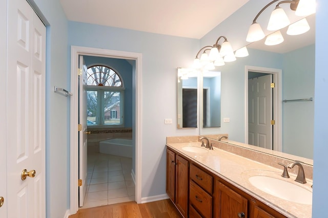 bathroom featuring a garden tub, double vanity, a sink, and baseboards