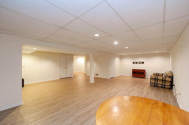 living area featuring light wood-type flooring, a paneled ceiling, and baseboards