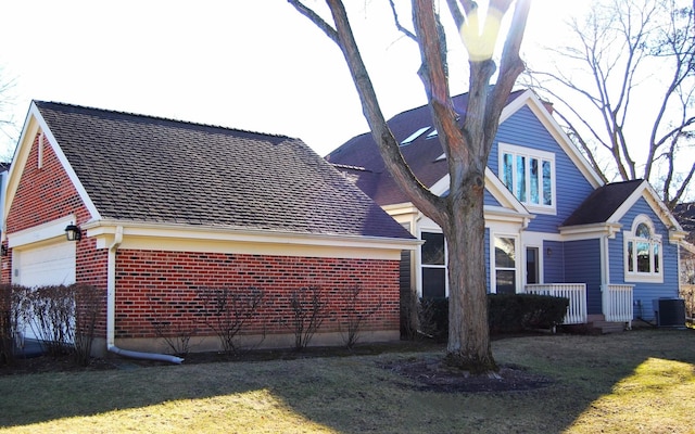 back of property featuring an attached garage, central AC, and brick siding