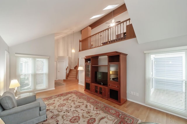 living room featuring ceiling fan, high vaulted ceiling, a skylight, light wood-style floors, and stairway