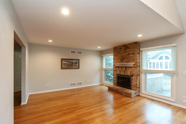 unfurnished living room featuring recessed lighting, visible vents, light wood-style floors, a brick fireplace, and baseboards