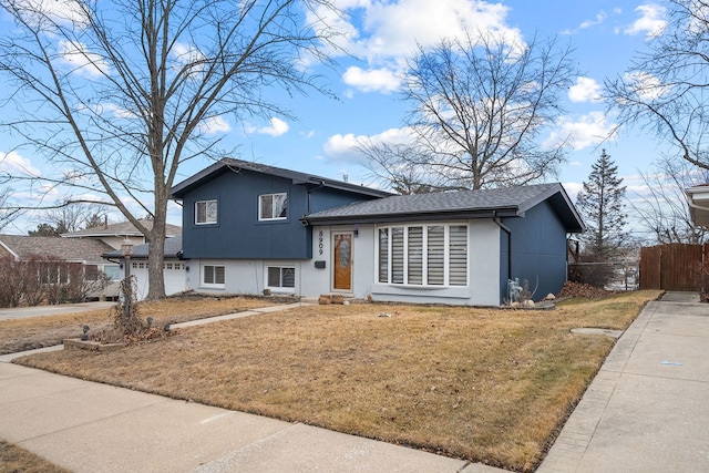 tri-level home featuring a garage, concrete driveway, fence, a front lawn, and stucco siding