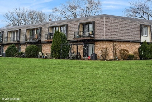 rear view of property featuring mansard roof, a lawn, a balcony, and brick siding