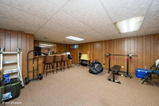 exercise room with bar, a drop ceiling, carpet flooring, and wooden walls