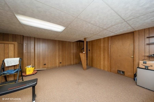 interior space with carpet floors, wooden walls, visible vents, and a paneled ceiling