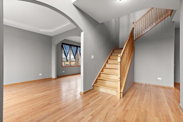 staircase with arched walkways, wood finished floors, and baseboards