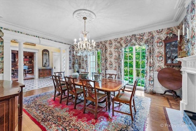 dining space featuring wallpapered walls, ornamental molding, a notable chandelier, and ornate columns