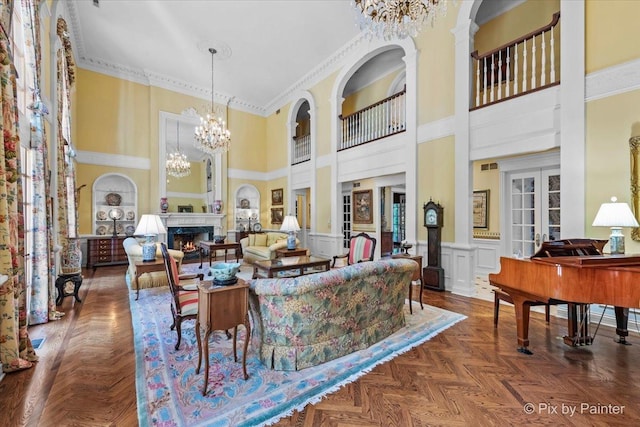 living area with a warm lit fireplace, crown molding, french doors, a chandelier, and a decorative wall