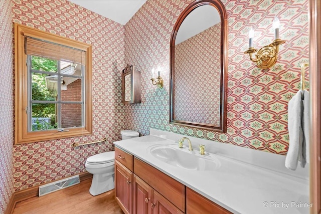 bathroom featuring toilet, wood finished floors, vanity, visible vents, and wallpapered walls