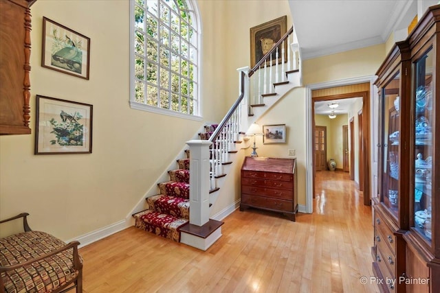 foyer featuring ornamental molding, light wood-type flooring, baseboards, and stairs