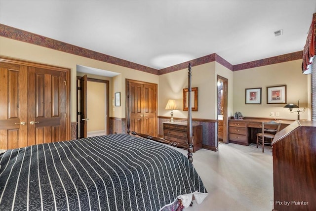 bedroom with light carpet, wainscoting, built in study area, and visible vents