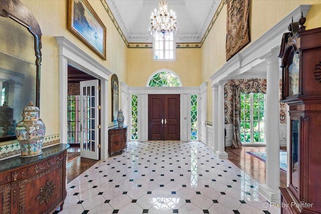 foyer entrance featuring a wainscoted wall, crown molding, a notable chandelier, decorative columns, and a decorative wall