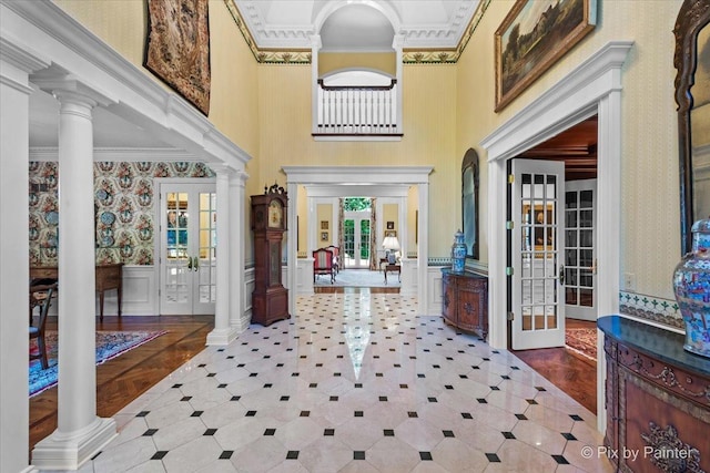 entrance foyer with wallpapered walls, decorative columns, wainscoting, crown molding, and french doors