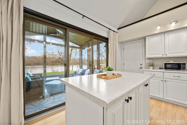 kitchen featuring a water view, light wood-type flooring, vaulted ceiling, white cabinetry, and light countertops