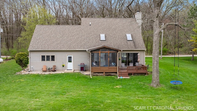 back of house featuring a chimney, a sunroom, roof with shingles, and a lawn