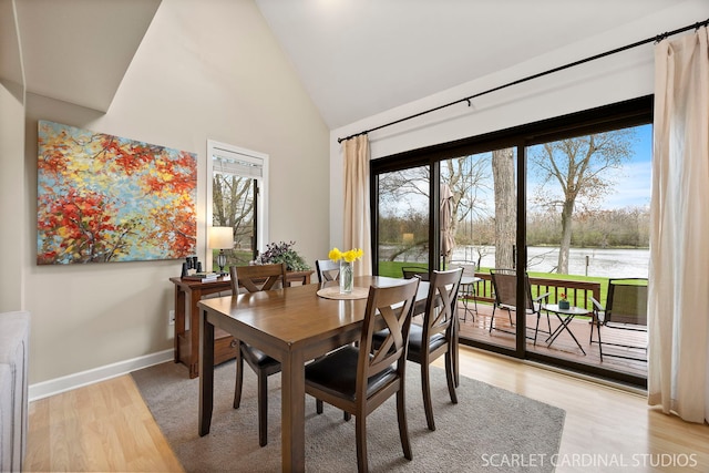 dining room featuring a wealth of natural light, light wood-style flooring, high vaulted ceiling, and a water view