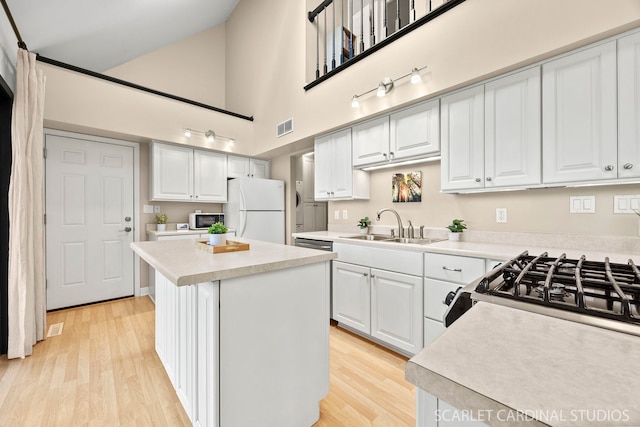 kitchen featuring a high ceiling, light countertops, visible vents, a sink, and freestanding refrigerator