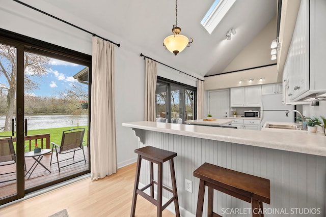 kitchen with a peninsula, a sink, a water view, light wood-type flooring, and light countertops
