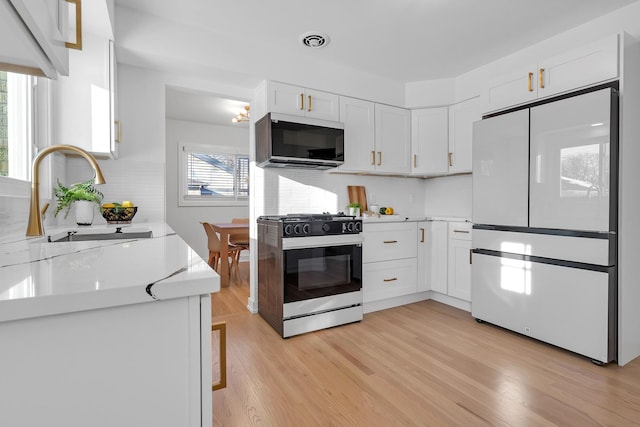 kitchen with light countertops, visible vents, refrigerator with glass door, a sink, and gas range