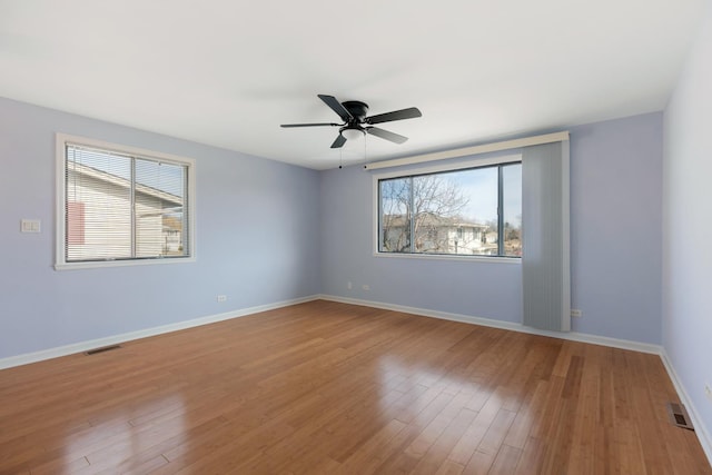 empty room with a wealth of natural light, visible vents, baseboards, and wood finished floors