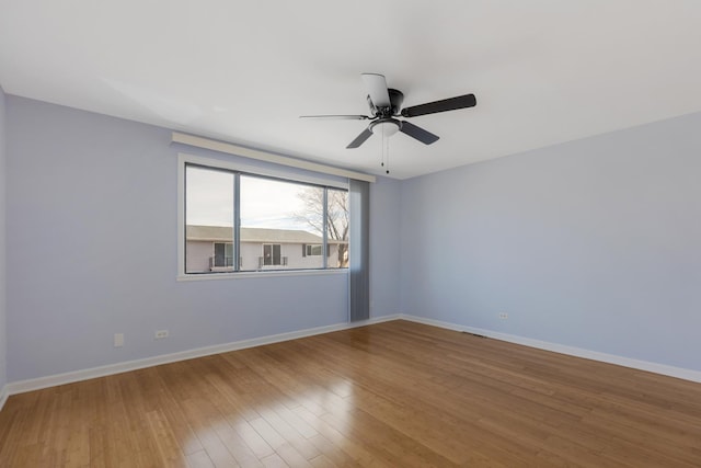 empty room with wood finished floors, a ceiling fan, and baseboards