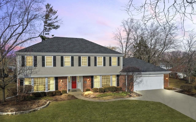 colonial inspired home featuring a garage, driveway, a shingled roof, a front lawn, and brick siding