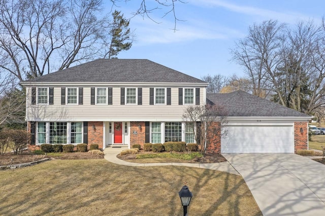 colonial inspired home featuring a garage, driveway, a shingled roof, brick siding, and a front yard