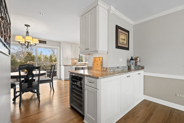 kitchen featuring wine cooler, dark wood-type flooring, baseboards, ornamental molding, and light stone countertops