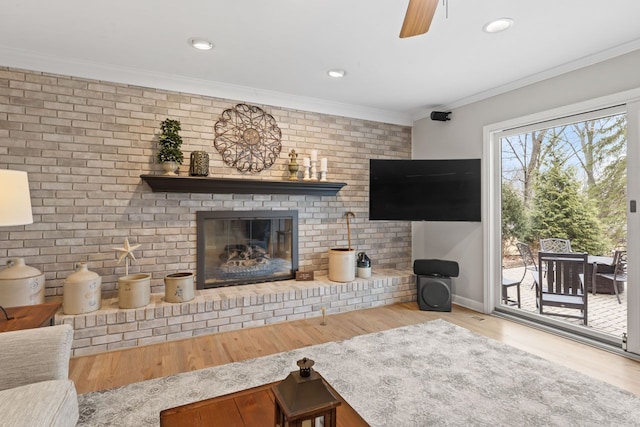 living area with brick wall, wood finished floors, crown molding, a brick fireplace, and recessed lighting