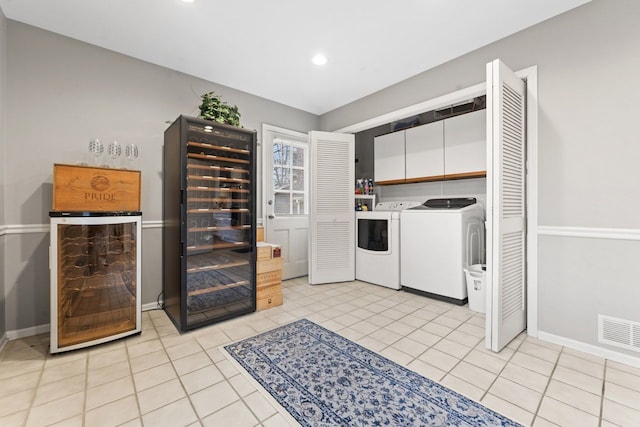 kitchen featuring light tile patterned floors, beverage cooler, visible vents, washer and dryer, and white cabinetry