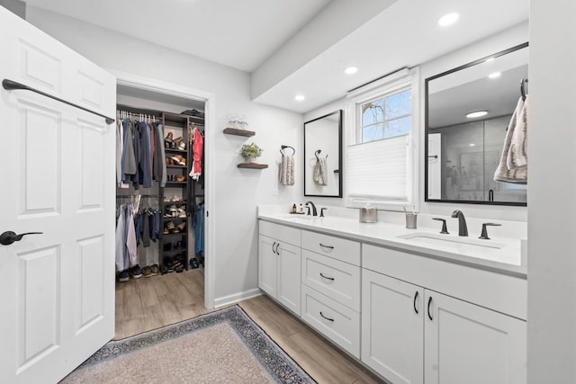 bathroom with double vanity, wood finished floors, a sink, and a walk in closet