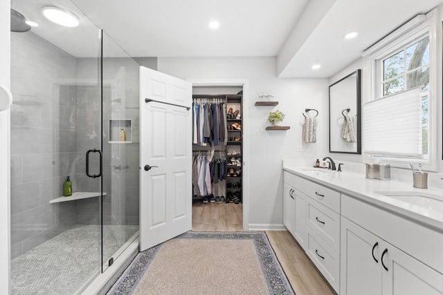 bathroom with a stall shower, double vanity, a sink, and wood finished floors