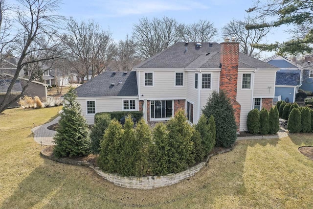 back of house with brick siding, a shingled roof, a chimney, and a yard