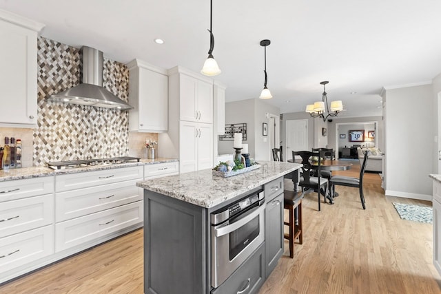 kitchen featuring light wood-type flooring, wall chimney range hood, appliances with stainless steel finishes, and white cabinets