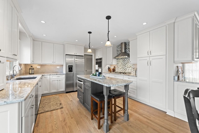 kitchen featuring wall chimney exhaust hood, appliances with stainless steel finishes, white cabinets, and a sink