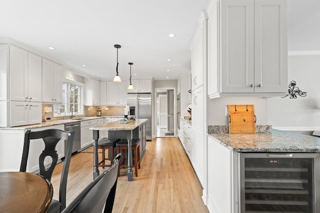 kitchen featuring beverage cooler, stainless steel appliances, light wood-style floors, a kitchen bar, and white cabinetry