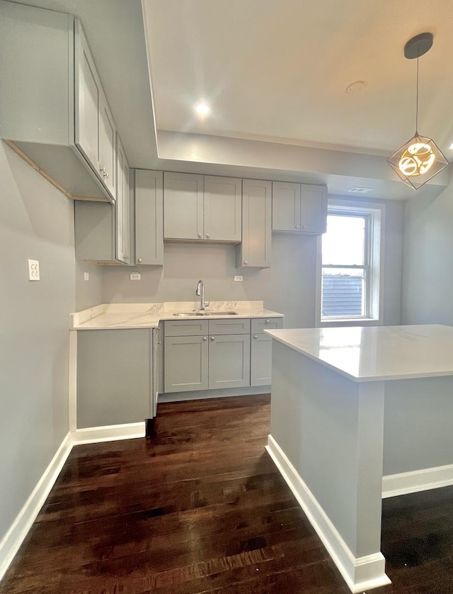 kitchen with pendant lighting, dark wood finished floors, light countertops, a sink, and baseboards