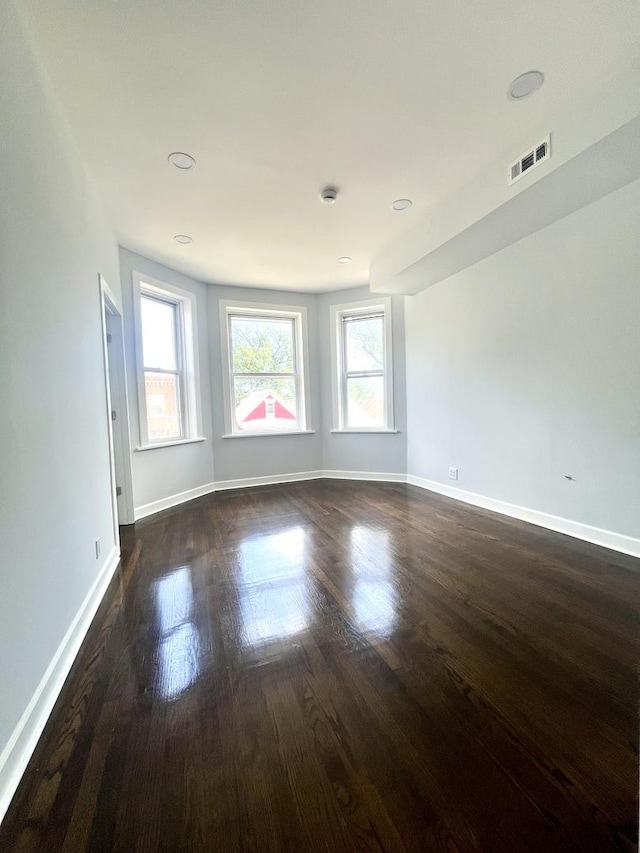 unfurnished room with baseboards, visible vents, and dark wood finished floors