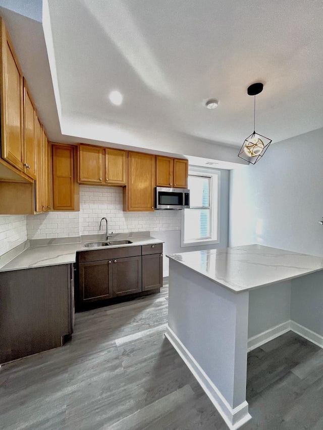 kitchen featuring stainless steel microwave, decorative backsplash, a sink, wood finished floors, and baseboards