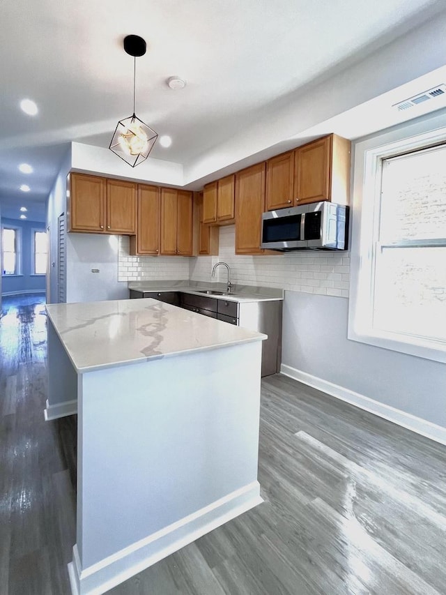 kitchen featuring brown cabinets, stainless steel microwave, visible vents, decorative backsplash, and a sink