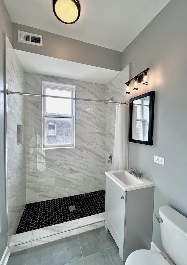 bathroom with visible vents, tiled shower, toilet, marble finish floor, and vanity