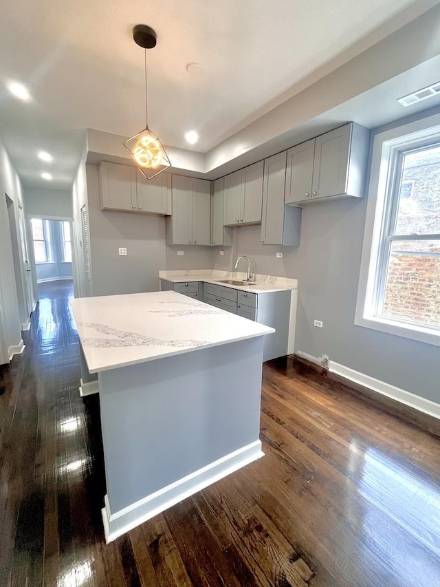 kitchen featuring dark wood-style floors, gray cabinets, a sink, and a center island