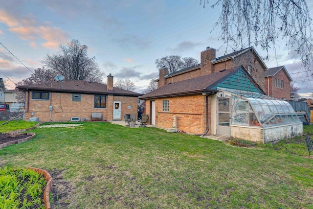 rear view of house featuring a yard, a greenhouse, an outdoor structure, and brick siding