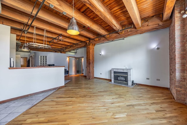 unfurnished living room with wooden ceiling, wood finished floors, beam ceiling, and a tile fireplace